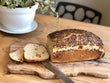 A loaf of artisan sourdough bread with Kumara and Flaxseed, cut into a slice, on a wooden board.