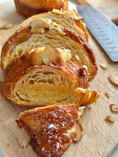 Sliced croissant on a wooden board with a knife in the background