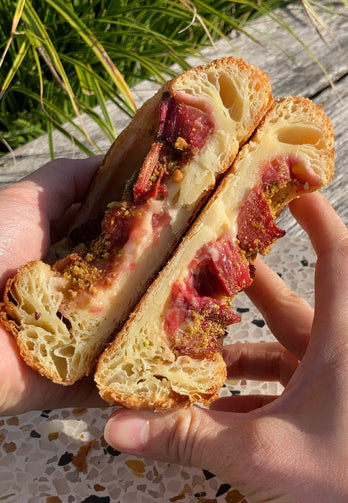 Hands holding a pastry that's been cut in half and showing the interior - rhubarb and custard 